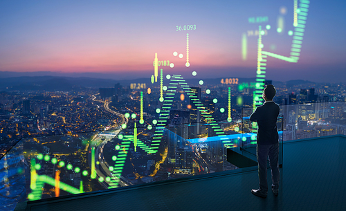 Businessman standing on open roof top balcony watching city night view with stock exchange market graph analysis background effect. Concept of stock market.